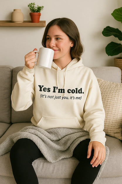 Woman wearing a hoodie with text, sitting on a couch holding a mug.