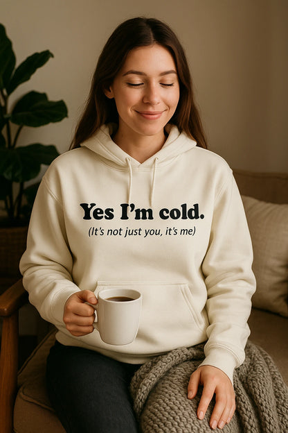 Woman wearing a hoodie with text holding a mug, sitting on a couch.